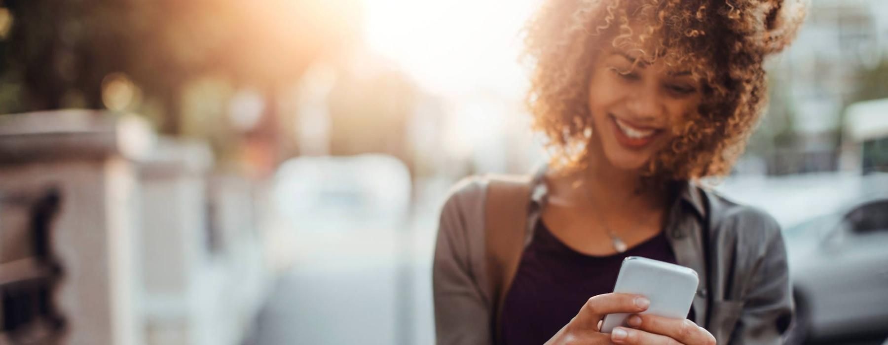 woman texts on her phone as she walks through the city